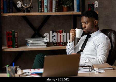 Serious junge afrikanische Geschäftsmann trinken Kaffee, während an einem Tisch im Büro sitzen Stockfoto