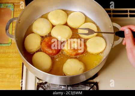 Frau dreht und fritiert runde Donuts in heißem Öl. Stockfoto