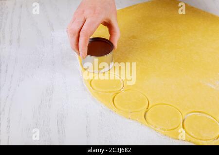 Frau schneidet Teigkreise aus, um Kekse auf dem weißen Tisch zu backen. Stockfoto