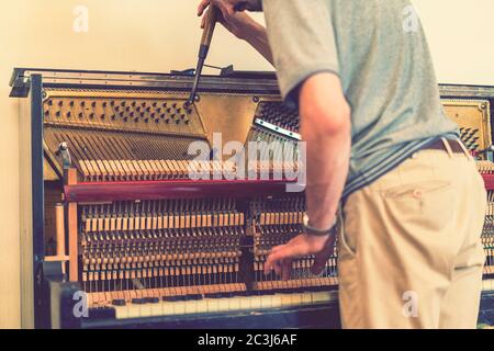 Klaviertuning-Prozess. Nahaufnahme der Hand und Werkzeuge des Tuners, der am Flügel arbeitet. Detailansicht des aufrechten Klaviers während einer Stimmung Stockfoto