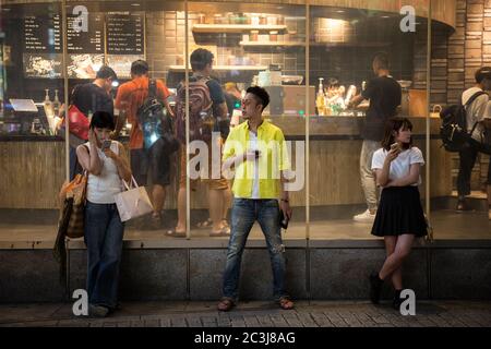 TOKIO, JAPAN - 26. JUNI 2016 - Junge Menschen mit ihren Handys, außerhalb von Starbucks in Shibuya Crossing, Tokio, Japan. Stockfoto