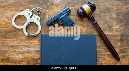 Gesetz, Verbrechen, Strafe Konzept. Richter-Gavel, Handfeuerwaffe, Handschellen und ein leeres Cover Rechtsbuch auf Holzschreibtisch Hintergrund, Draufsicht, Kopierraum. Stockfoto