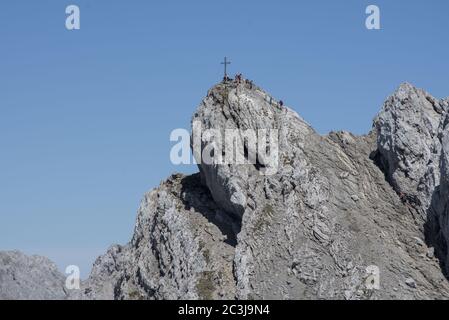 Gipfelkreuz der Westkarwendelspitze mit ruhenden Wanderern, gelegen im Karwendelgebirge bei Mittenwald, Deutschland Stockfoto