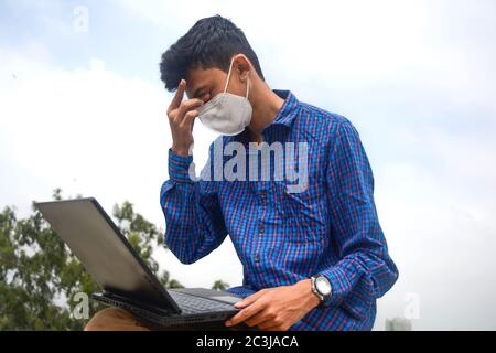 Teen Mann arbeiten in Laptop und suchen streßreich.man mit schützenden Gesichtsmaske Stockfoto