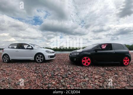 Moskau, Russland - 03. Mai 2019: Zwei Spielzeugautos Volkswagen Golf mk6 stehen auf einem Kiesstrand des Flusses Moskau. Weiße und schwarze GTI stehen einander gegenüber Stockfoto