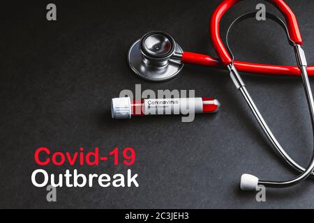 COVID-19-AUSBRUCHSTEXT mit Stethoskop und Blutprobenvakuumschlauch auf schwarzem Hintergrund. Covid oder Coronavirus Konzept Stockfoto