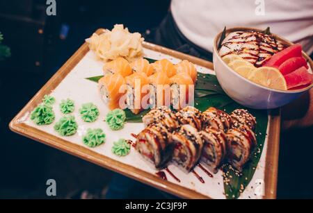 Nahaufnahme Hand Kellner Holding Set köstliche frische Sushi Schieferteller Sushi Rolls Warm Sake Unagi, japanischer roher Fisch in traditionellem Restaurant. Philadelp Stockfoto