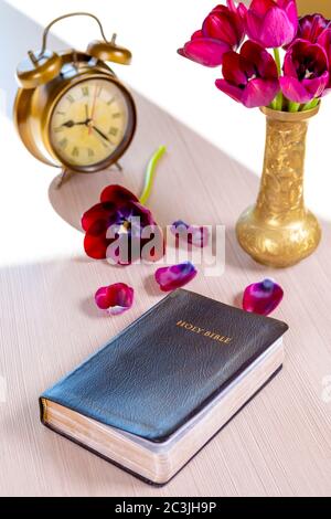 Heilige Bibel und alter Goldrundwecker mit Blumen auf Holztisch Hintergrund. Zeit für Studium, Lesen und Spiritualität Konzept. Stockfoto