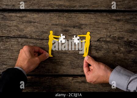 Zwei Geschäftsleute mit Papier Ausschnitt Silhouetten von Männern halten Puzzle-Stücke auf rustikalem Holz. Stockfoto