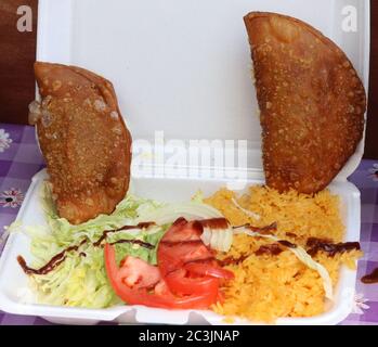 Käse und Fleisch Empanadas mit Salat, Tomaten, gelbem Reis und Sauce auf Styropor Lebensmittelbehälter Stockfoto