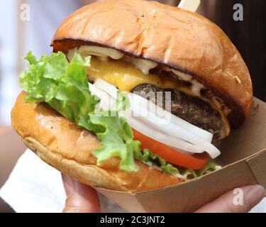 Saftiger Cheeseburger mit Salat, weißer Zwiebel, Tomate auf einem Brötchen in einer Pappschachtel Stockfoto