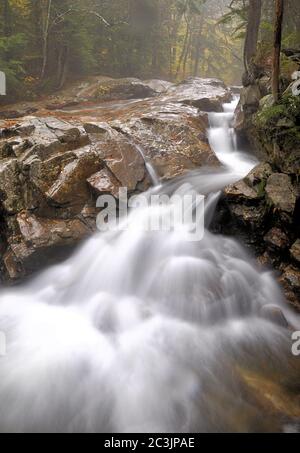 Herbst im Franconia Notch State Park in New Hampshire. Nebel steigt aus dem wunderschönen Wasserfall, während Pemigewasset River seinen Weg durch Granitfelsen streichelt. Stockfoto