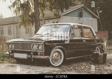 Altes Retro-Auto auf dem Hintergrund der Scheune im Dorf. Auto mit weißen Reifen..in der Nähe ist ein alter Lederkoffer. Um den Wald herum Stockfoto