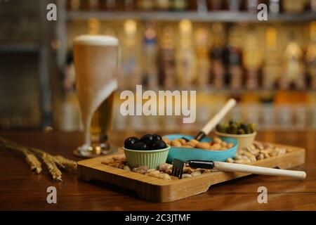Ein Glas Bier auf dem Tisch der Bar mit Verschiedene Arten von Oliven und Getreide auf der Seite Stockfoto
