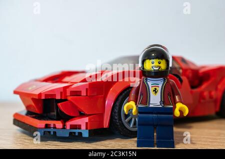 POZNAN, POLEN - 01. Mai 2020: LEGO Profi-Fahrer mit Helm vor einem roten Ferrari Rennwagen in weichem Fokus Hintergrund stehen. Stockfoto