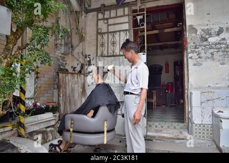 GUANGZHOU, CHINA – CA. MAI 2020: Ein Straßenbarbier arbeitet täglich vor seinem Haus im alten Stadtteil. Stockfoto