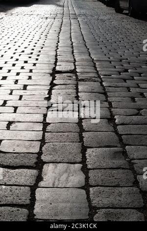 Pflastersteine im Gegenlicht. Eine gepflasterte Straße, die sich in die Ferne zieht. Nahaufnahme Stockfoto