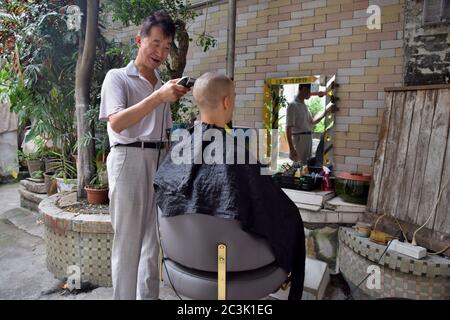 GUANGZHOU, CHINA – CA. MAI 2020: Ein Straßenbarbier arbeitet täglich vor seinem Haus im alten Stadtteil. Stockfoto