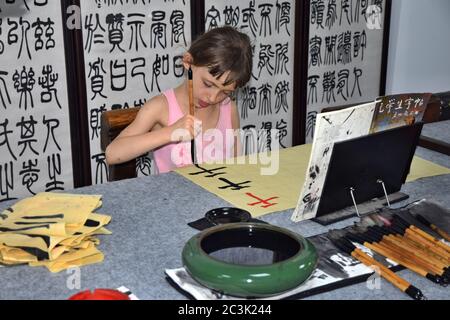 GUANGZHOU, CHINA - CIRCA JUNI 2020: Ein kleines weißes Mädchen in der Lektion der chinesischen Kalligraphie. Die Übersetzung der Zeichen: Zahlen. Stockfoto