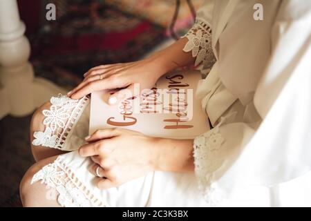 Junge Frau in weißem Kleid sitzt und hält geschlossen weißes Buch auf ihrem Schoß. Text auf Buchcover: Auf Wiedersehen Miss ... Hallo Frau Hochzeitstag Konzept. Stockfoto