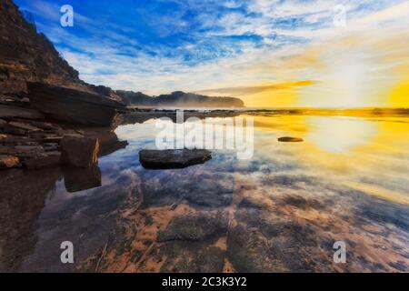 Strahlende Sonne über dem pazifischen Ozeanhorizont am Turimetta Strand von Sydney Nordstrände spiegeln sich in der Ebbe Meeresboden Küste. Stockfoto