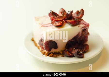 Japanische Käsekuchen mit Kirschsauce und frischen Kirschen auf der Keramikplatte und rotem Hintergrund, süßes Dessert Stockfoto