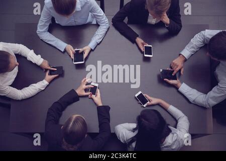 Geschäftsleute mit leeren Telefonen, die mit der App um den Tisch sitzen, Draufsicht Stockfoto