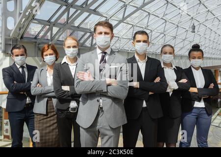 Geschäftsleute tragen schützende chirurgische Masken und stehen zusammen mit Armen gekreuzt, Gesundheitswesen und covid-19 Präventionskonzept Stockfoto