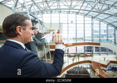 Team von Geschäftsleuten, die Papierflugzeuge in einem modernen Bürogebäude zusammenwerfen Stockfoto