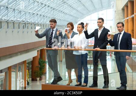Team von Geschäftsleuten, die Papierflugzeuge in einem modernen Bürogebäude zusammenwerfen Stockfoto