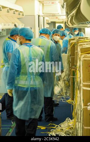 Chinesische Lader tragen Hazmat Anzüge Laden eines umgebauten Fahrgastes in Frachtschiff Flugzeug mit chirurgischen Masken und Kleider zu kämpfen COVID-Pandemie Stockfoto