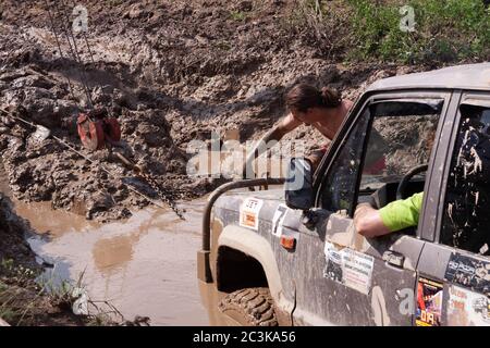 Moskau, Russland - 25. Mai 2019: Ein Mann befestigt eine Kette an einem Auto, das im Schlamm steckt. Off-Road und isuzy Trooper SUV stecken in einem tiefen Loch. Stockfoto