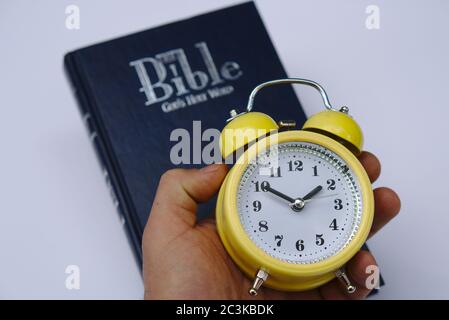 Person, die einen Wecker mit der Bibel in der hält Hintergrund Stockfoto