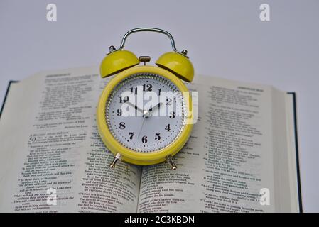 Gelber Wecker auf der offenen Bibel auf einem weißen Oberfläche Stockfoto