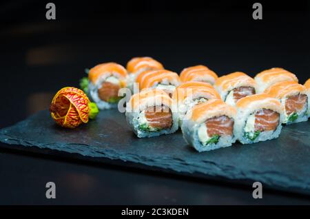 Sushi, traditionelle japanische Küche. Leckeres Uramaki auf dekorierten Teller, schwarzer Hintergrund. Stockfoto