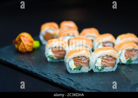 Sushi, traditionelle japanische Küche. Leckeres Uramaki auf dekorierten Teller, schwarzer Hintergrund. Stockfoto