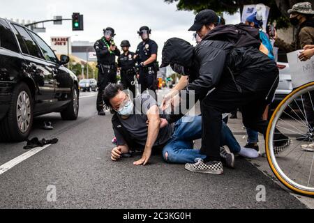 Ein Protestant in Los Angeles wird nach dem Schiebe auf den Boden von einem Offizier geholfen. Man sieht einen Offizier, der mit einer nicht-tödlichen Waffe auf ihn zielt. Stockfoto