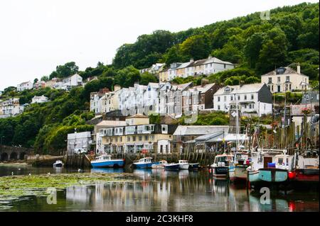 Segelboote auf dem Wasser und die Häuser auf einem baumbedeckten Hügel gefangen in Polperro Beach, Großbritannien Stockfoto