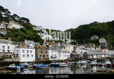 Segelboote auf dem Wasser und die Häuser auf einem baumbedeckten Hügel gefangen in Polperro Beach, Großbritannien Stockfoto