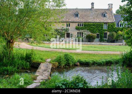 Bauernhaus und Steinfußbrücke über das Flussauge am frühen Morgen. Upper Slaughter, Cotswolds, Gloucestershire, England Stockfoto