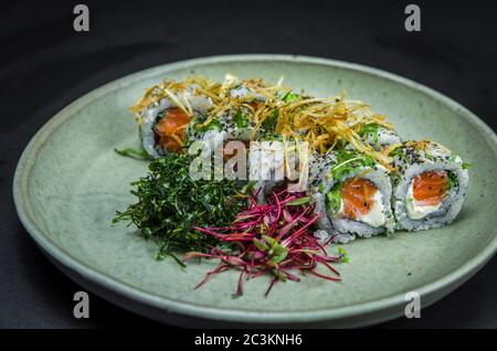 Sushi, traditionelle japanische Küche. Leckeres Uramaki auf dekorierten Teller, schwarzer Hintergrund. Stockfoto