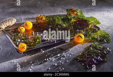 Knusprige Nori-Algen mit Kirschtomaten und dunklen Gewürzen auf grauem Beton. Japanisches Essen Nori. Getrocknete Blätter von Algen. Speicherplatz kopieren. Stockfoto