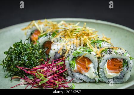 Sushi, traditionelle japanische Küche. Leckeres Uramaki auf dekorierten Teller, schwarzer Hintergrund. Stockfoto