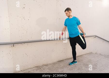 Junger Mann Läufer immer bereit zu laufen Stretching Beine wärmen Quad Stretch Übung auf Außentreppe Stockfoto