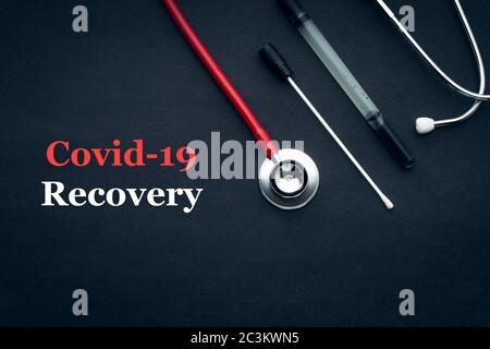 COVID-19 oder CORONAVIRUS RECOVERY Text mit Stethoskop und medizinischem Tupfer schwarzem Hintergrund. Covid-19 oder Coronavirus Konzept. Stockfoto