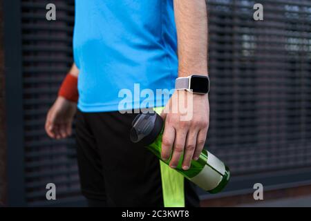 Beschnittenes Bild eines sportlichen Mannes mit einer Flasche Wasser in der Hand und einer Sport-Smartwatch am Handgelenk Stockfoto