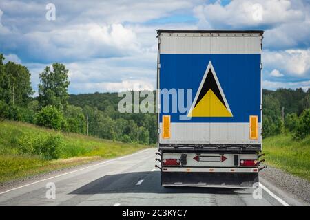Ein LKW mit der Nationalflagge von St. Lucia, die auf der Hintertür abgebildet ist, transportiert Waren in ein anderes Land entlang der Autobahn. Konzept von Export-Import Stockfoto