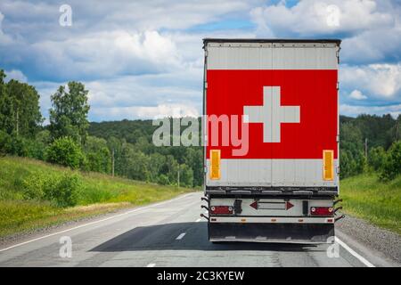 Ein LKW mit der Nationalflagge der Schweiz auf der Hintertür trägt Waren in ein anderes Land entlang der Autobahn. Konzept Export-Import, Stockfoto