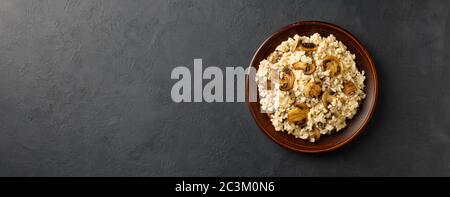 Traditionelle italienische Küche - vegetarisches Risotto mit Pilzen. Schwarzer Stein hinten. Restaurant oder Cafe Menü Konzept. Langes Bannerformat. Stockfoto