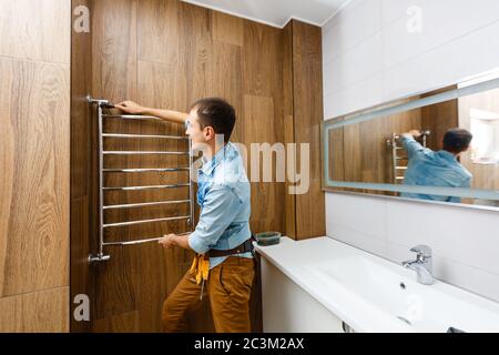 Klempner installiert Handtuchwärmer an der Wand im Bad. Stockfoto